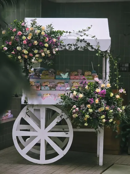 A charming white cart adorned with flowers, used as a gift or dessert station for the baby shower. It's a whimsical detail that adds to the overall theme.