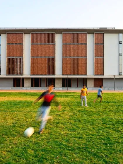 The grounds of the JSW School of Public Policy at IIM Ahmedabad provide ample space for recreation and relaxation. The building's facade, with its pattern of solid and void, serves as a backdrop to the active campus life.