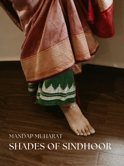 A detail shot showing the layered effect of wearing a family heirloom. Here, the bride wears her grandmother's green chaniya underneath a beautiful red saree for her Mandap Muharat, a subtle yet powerful nod to her roots.