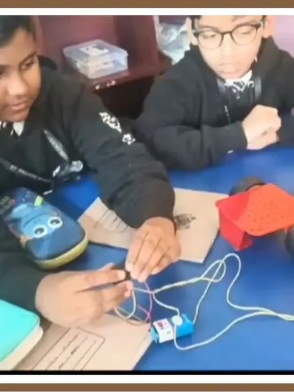 A close-up shot of students assembling a robotic car. This image captures the focus and teamwork involved in connecting wires to a battery and motor, a fundamental step in bringing their creations to life.