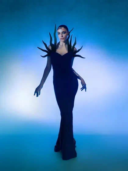 A full-length view of the conceptual gown, showing how the sculptural elements transform the human form. The lighting creates a gradient effect, adding to the otherworldly atmosphere.