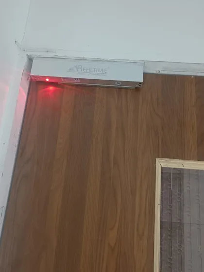 A Realtime EM lock installed on a wooden door, showing its versatility for different door types. The red light indicates the lock is powered and active.