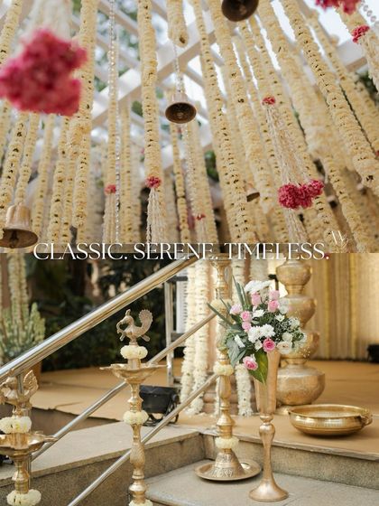 Classic, serene, and timeless. This image captures the essence of the wedding ceremony, with traditional brass lamps at the entrance of an aisle leading to a mandap adorned with fragrant florals.
