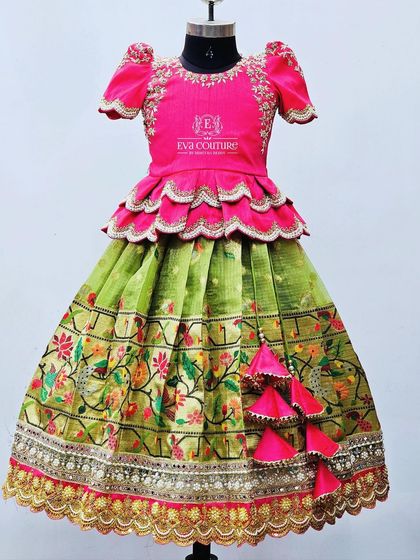A grand Paithani-style lehenga with a pink tiered peplum blouse and a green skirt with a heavily embroidered peacock and floral border.