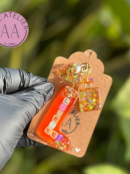 The 'Loveet' initial keychain, held up to show the details. The letter 'L' is filled with glitter and the name, creating a special and personal item.