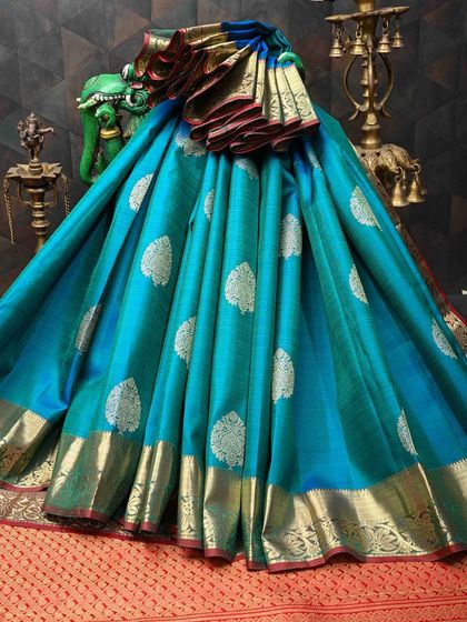 This turquoise Kanjivaram silk saree is a vision of elegance. The body is covered in silver leaf motifs, and the contrasting gold border adds a warm glow. It’s a unique color that is sure to turn heads.