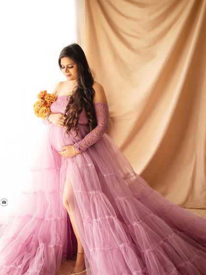 A side profile of a mother-to-be in a flowing lavender gown, holding a bouquet of orange flowers that add a lovely pop of color.