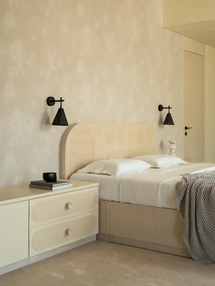 The master suite in the 'Soft Serve' project is enveloped in a timeless taupe. The custom bed and vanity feature abstract patterns in Movingue White veneer, with scalloped motifs framing the bay window.