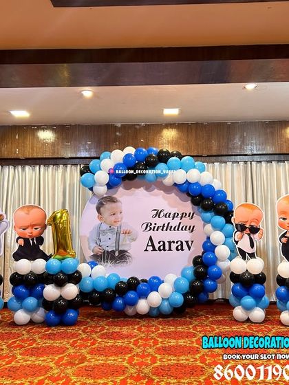 Aarav's Boss Baby themed first birthday party. This hall setup includes a round photo backdrop, a blue, black, and white balloon garland, and multiple character cutouts.