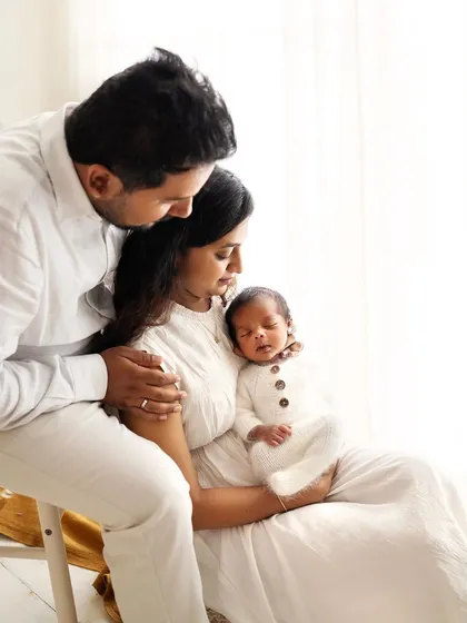 The new family of three, all dressed in white, admiring their little one. The soft, natural light creates a beautiful, airy feel.