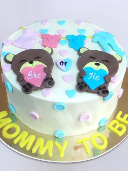 This "Mommy to Be" cake features two sweet bears holding "She" and "He" hearts, with a clothesline of baby clothes on top.