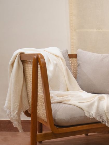 A detail shot of my teak and rattan armchair, draped with a soft throw. The smooth curve of the armrest and the texture of the cane work together to create a tactile experience.