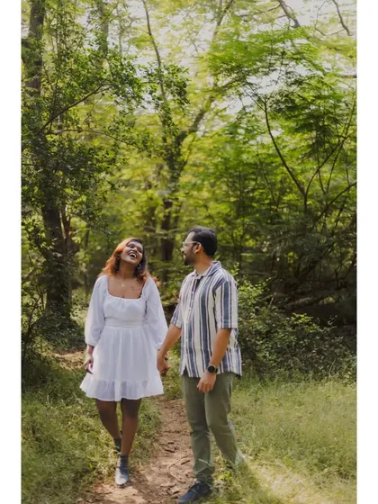 A joyful, candid photo of Hanish and Gloria walking hand-in-hand through a sunlit forest path during their pre-wedding shoot.