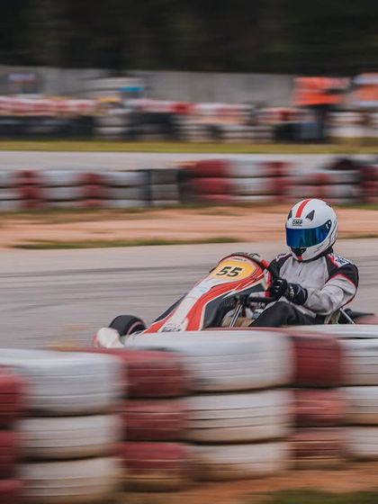 A driver in a white and red kart speeds past the tyre wall.