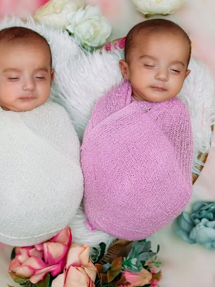 Two peas in a pod. These newborn twins are swaddled and sleeping side-by-side in a basket, surrounded by a soft bed of flowers, creating a dreamy and artistic portrait.