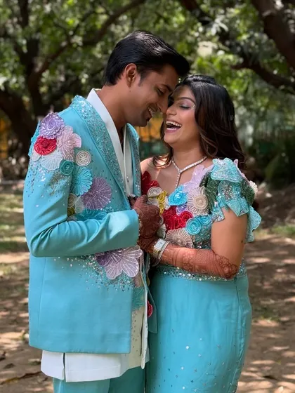 A candid moment from a carnival-themed event. The makeup is fresh and radiant, designed to complement the vibrant, floral-themed outfits of the happy couple.