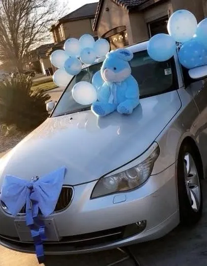 A car decorated with a large blue bow and light blue balloons to celebrate the arrival of a baby boy.