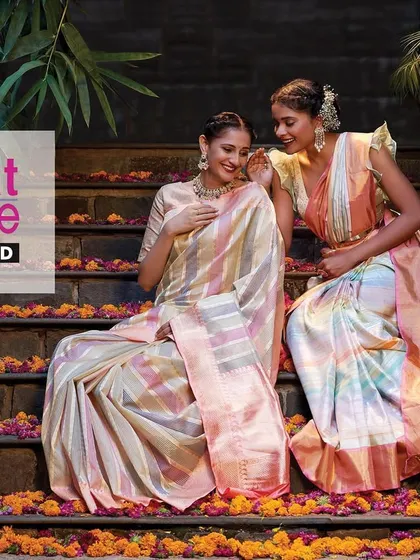 A campaign shot for Kasat Exclusive featuring their stunning sarees. The models are posed on stone steps adorned with flowers, creating a scene that is both traditional and contemporary.