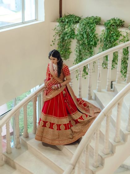 A graceful portrait of the bride descending a staircase, her red lehenga spread beautifully. It's a classic and elegant bridal shot.