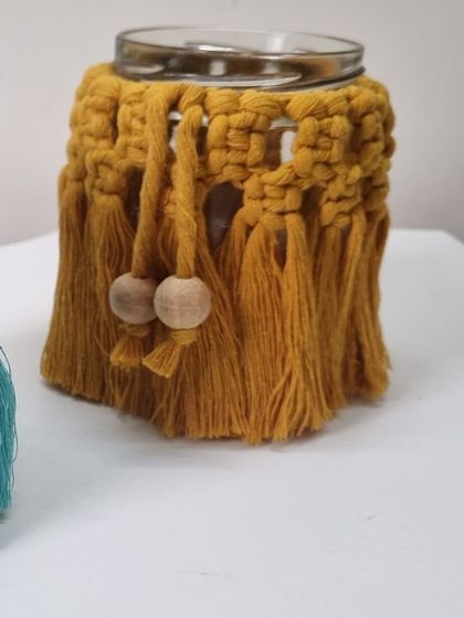 A mustard yellow macrame jar cover, detailed with wooden beads for an extra touch of natural charm.