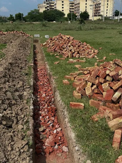 Broken brick aggregate (rodi) being laid in the foundation trenches. This is a standard construction practice to create a stable and level base before pouring the concrete footing.