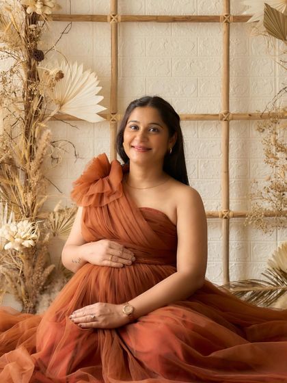 A happy and glowing portrait of a mama-to-be. The Copper gown's one-shoulder design and the boho backdrop create a warm and inviting photo.
