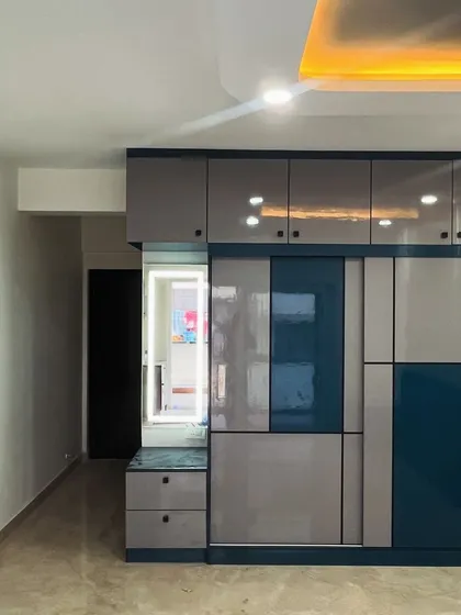 Color combinations and patterns play a vital role in design. This sliding wardrobe features a geometric pattern using grey and blue high-gloss laminates, paired with a built-in dresser with a backlit mirror.