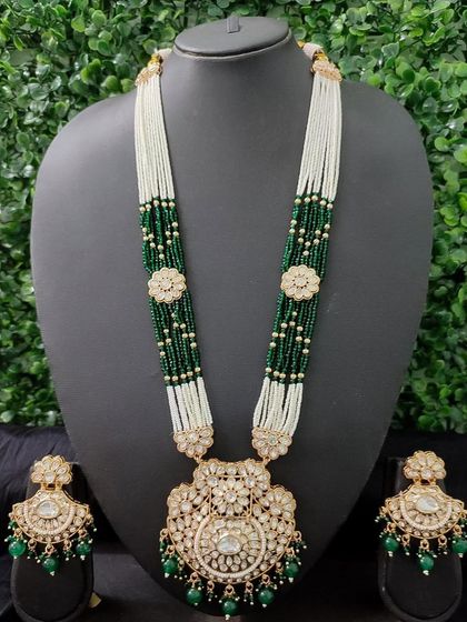 A magnificent long necklace set for rent, featuring a large kundan pendant and matching earrings. The green and white pearl beadwork adds a touch of royalty.