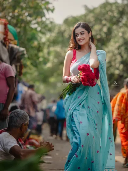 A model in a light blue saree stands in the middle of a vibrant Kolkata flower market. This environmental portrait captures the contrast between her serene presence and the lively background.