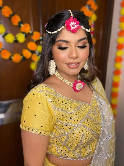 Simran in her blushing bridal glow for her mehendi. The look is fresh and vibrant, with a pop of pink on the lips to match her floral jewelry.