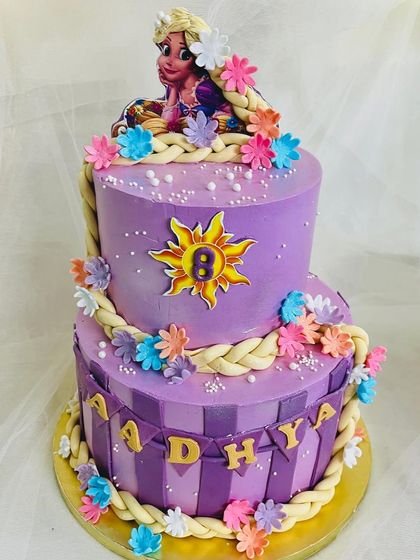 A two-tier Rapunzel cake with her long, braided hair cascading down the sides. The purple cake is decorated with the floating lantern sun symbol and colorful flowers from her story.