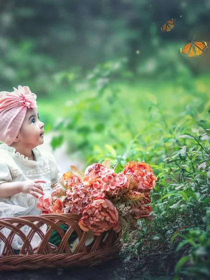 A curious baby girl in a basket looks up at butterflies against a backdrop of lush greenery. The soft, dreamy light gives this portrait an ethereal quality.