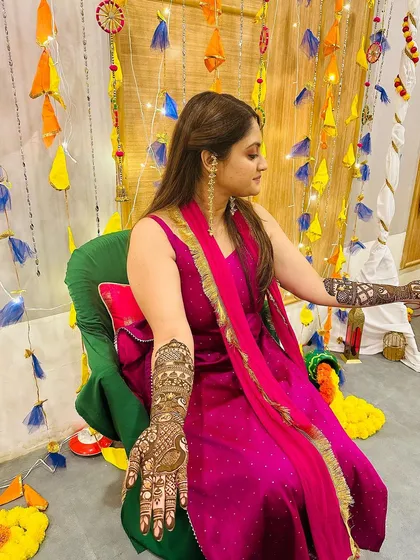 A client looking regal in a magenta outfit, her arms decorated with full-coverage traditional mehndi for her special event.