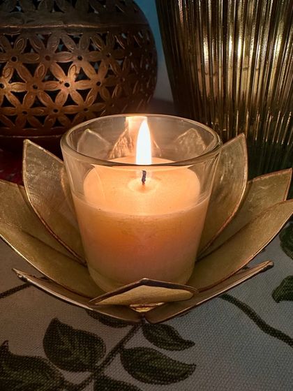 A close-up of a lit votive candle in a lotus holder. Sometimes, all you need is the simple glow of a favorite fragrance to unwind.
