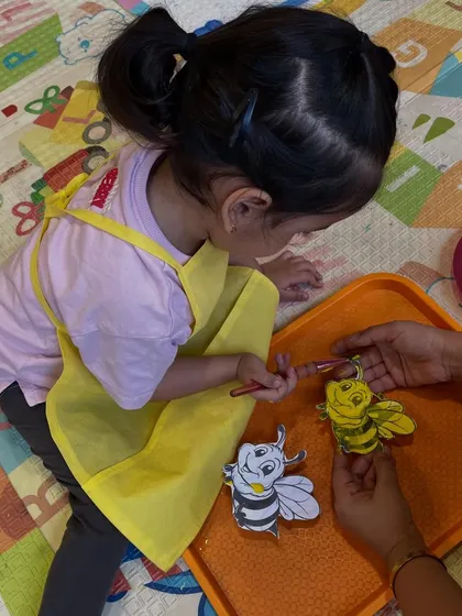 A close-up of a toddler carefully painting her bee cutout. I provide assistance when needed, but the focus is always on letting the child lead their own creative process.
