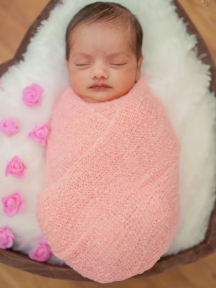 This tight shot focuses on the baby's face, capturing the peacefulness of sleep. The soft white fur lining provides a gentle contrast to the warm pink wrap.