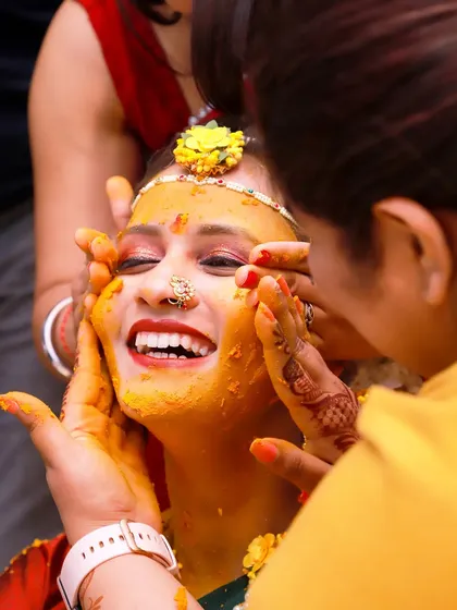 A candid shot capturing the pure joy of a bride during her Haldi ceremony, her face lit up with a wide smile as family applies turmeric paste. These unscripted moments of happiness are what make wedding photography so special.