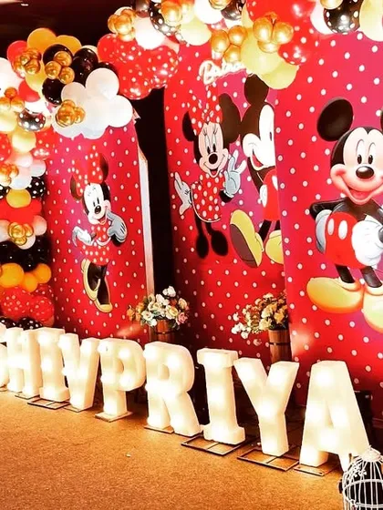 A fun and festive Mickey and Minnie Mouse themed birthday party for Shivpriya. The backdrop features the iconic characters, surrounded by a balloon arch in the classic red, yellow, and black color scheme.