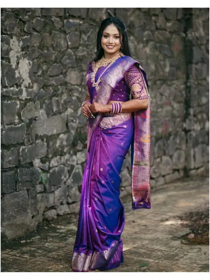 A full-length portrait of Ashlesha, highlighting the magnificent drape and design of her purple Paithani saree against a classic stone wall backdrop.