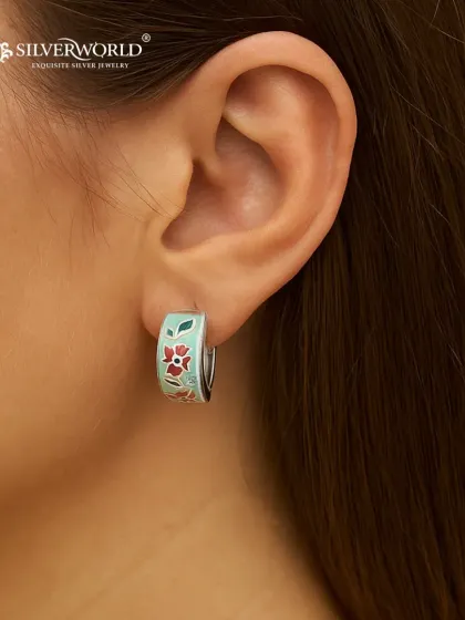 Our floral enamel hoop earrings are perfect for adding a pop of color. The delicate red and green floral pattern is hand-painted onto a silver base, creating a cheerful and stylish accessory.