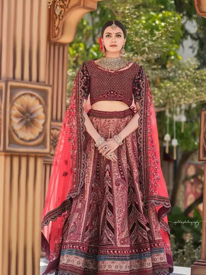 A modern bride in a stunning, intricately embroidered lehenga. The outdoor setting with architectural elements provides a beautiful contrast to the detailed outfit.