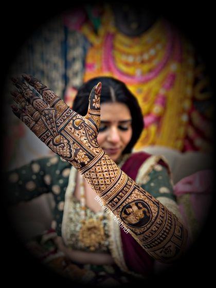 A bride showcasing her full-arm mehndi. This design includes intricate figures and patterns, a hallmark of our advanced bridal work.