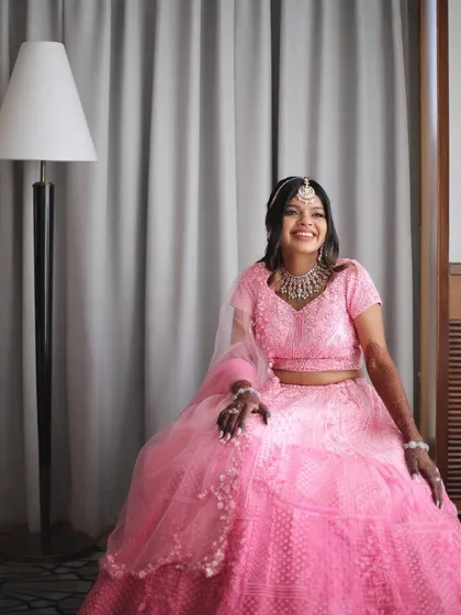 A happy and relaxed portrait of the bride. Her makeup is soft and pretty, with a focus on rosy cheeks and a bright smile, perfectly matching the cheerful pink of her wedding dress.
