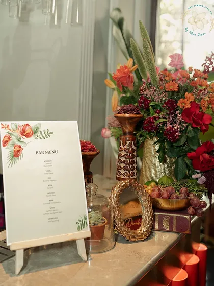 A beautifully styled bar menu on a small easel, flanked by a lush floral arrangement. This shows our commitment to making even the most functional elements of an event aesthetically pleasing.