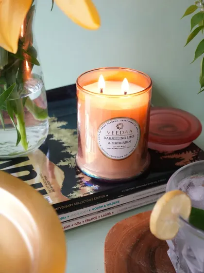 The warm glow of our Darjeeling Lime & Mandarin two-wick candle creates an inviting atmosphere. The hand-cut glass jar adds a touch of sophistication to this cozy, relaxing scene.