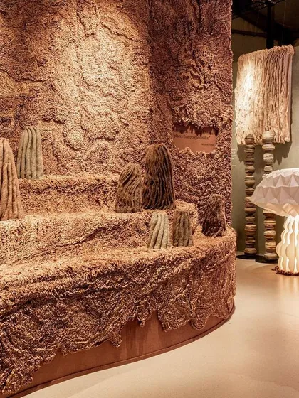 Another view of the 'Shroom' installation, showing the landscape of textured forms alongside glowing, paper-folded mushroom lamps. The space is a study in organic shapes and diffused light.