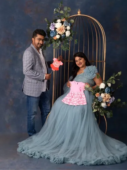 A fun and sweet announcement shot. The couple holds up tiny pink clothes, hinting at the arrival of a baby girl, all within our elegant cage setup.