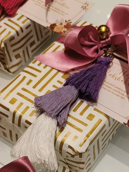A beautifully wrapped gift sets the tone for what's inside. This present features a geometric gold and white paper, a rich satin ribbon, and a multi-colored tassel charm, making the act of unwrapping a delight.