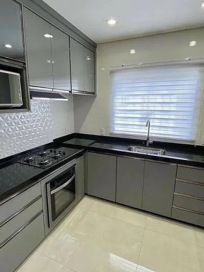 This angle showcases the cooking zone with a hob and built-in oven. The glossy grey cabinets and textured white backsplash create a modern and visually interesting kitchen space.