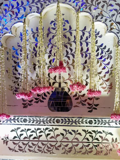 A detail of the stage backdrop, featuring intricate mirror-work panels with hanging floral tassels. This element combines traditional craftsmanship with floral artistry.